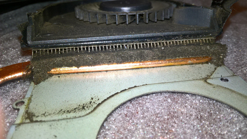 Zanieczyszczony radiator i wentylator chłodzenia laptopa, widoczne nagromadzenie kurzu i brudu na elementach chłodzących, miedziana rurka cieplna, drobne żeberka radiatora.