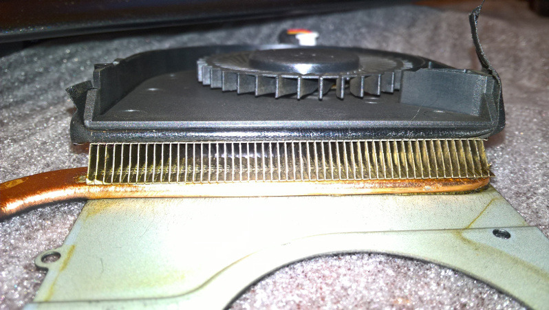 Detail laptop cooling system after cleaning, showing heatsink fins, copper heat pipe, and fan assembly with visible dust residue and thermal paste marks.