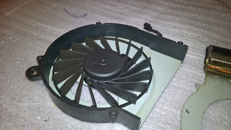 Wyczyszczony wentylator laptopa z widocznym radiatorem, gotowy do ponownego montażu, leżący na szorstkiej powierzchni.