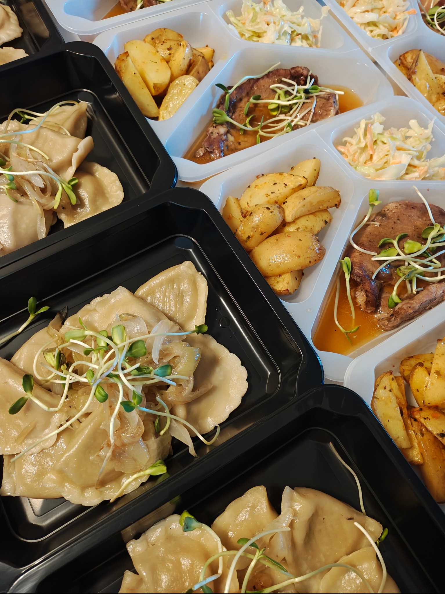 Zestaw obiadowy w pojemnikach: pierogi z cebulką i kiełkami, pieczone ziemniaki, surówka i mięso w sosie. Gotowe dania na wynos, catering.