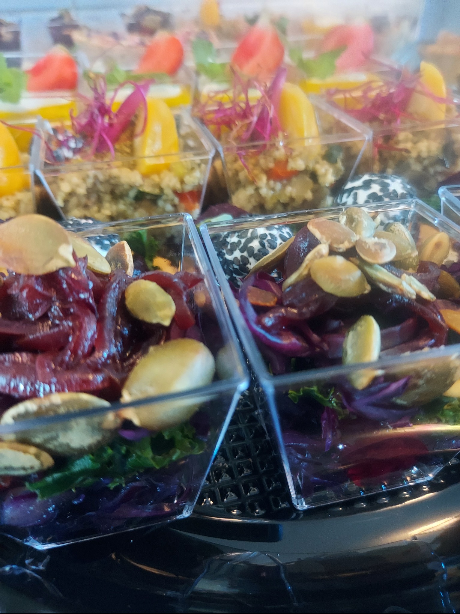 Eleganckie, przezroczyste pojemniki z cateringiem: sałatka z buraków, pestki dyni w pierwszym planie, w tle kasza z mango i truskawkami.