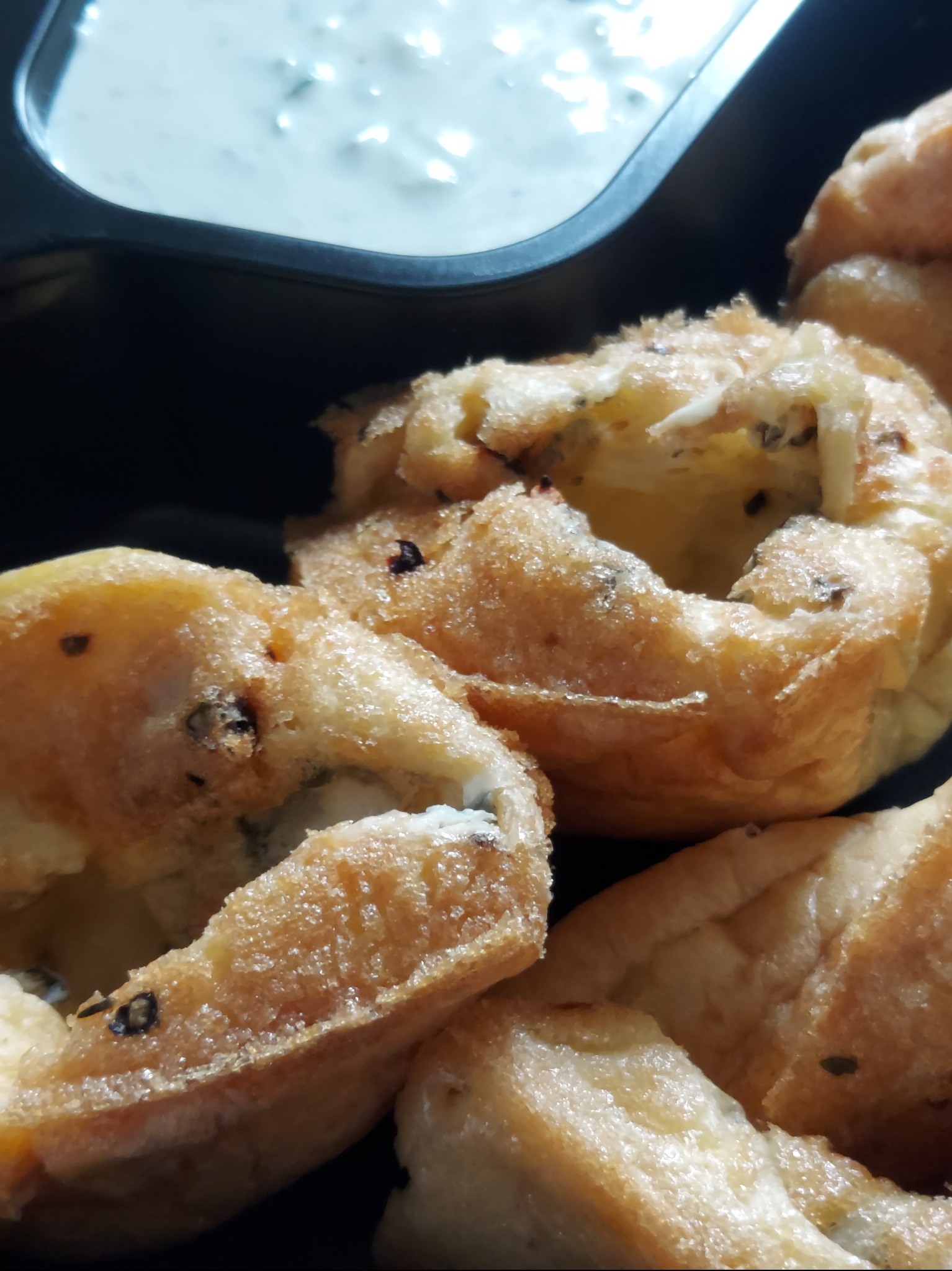 Makro zbliżenie na złociste, pieczone obwarzanki z ziołami, podane z kremowym sosem w czarnym naczyniu, sugerujące wykwintny catering na imprezę.