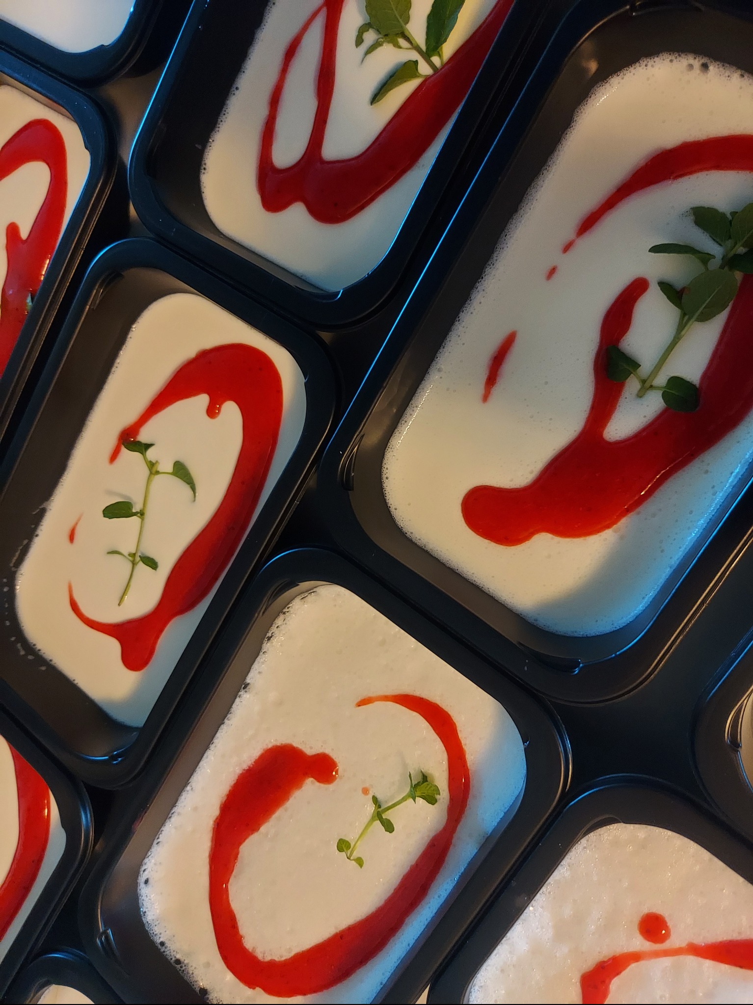 Deser w czarnych pojemnikach: biała pianka, dekoracja z czerwonego sosu i zielonego listka. Elegancki catering na imprezę firmową.