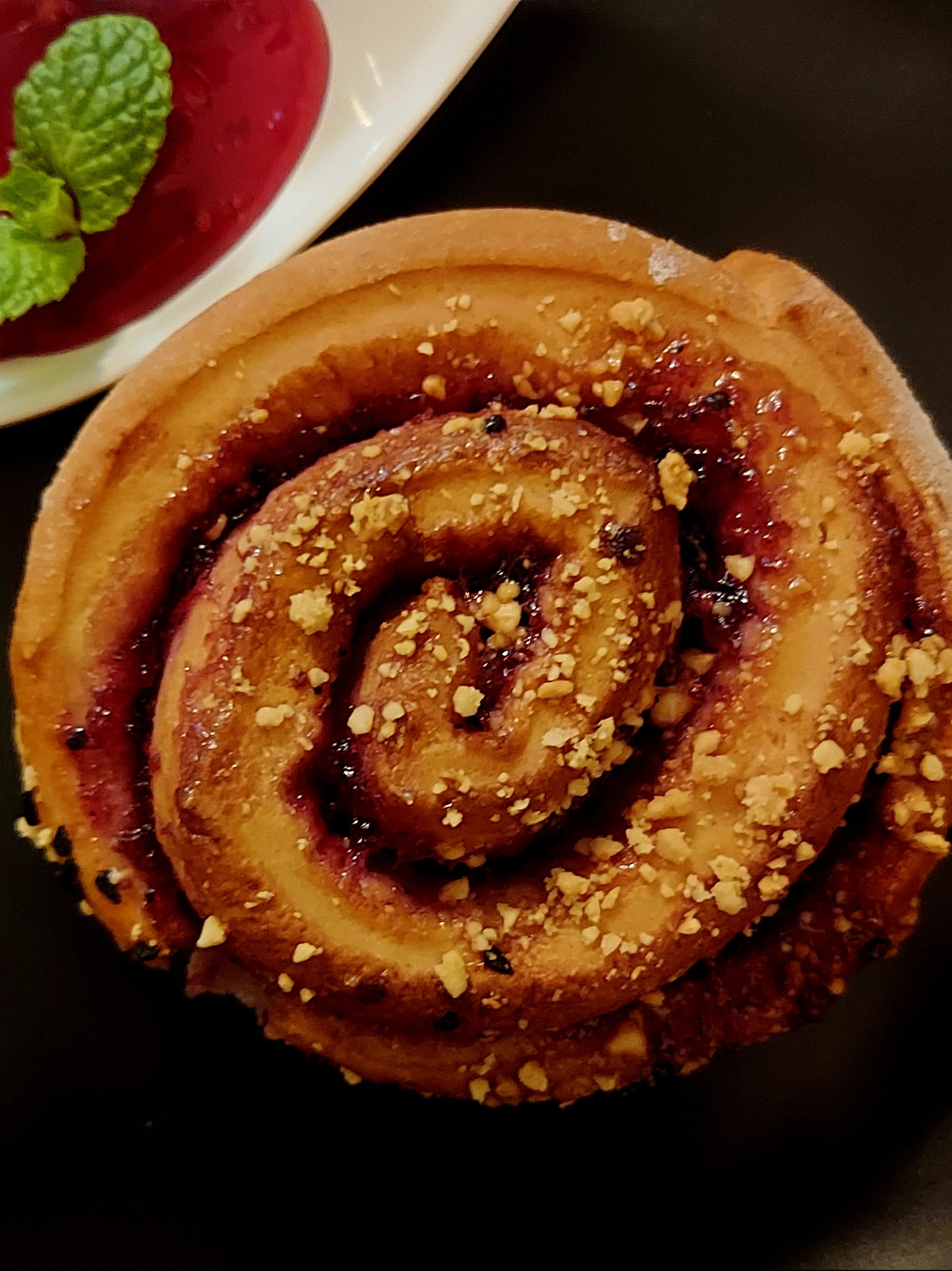 Cynamonka z jagodami i posypką z orzechów na czarnym tle. Obok sos malinowy z miętą. Elegancki deser na catering.