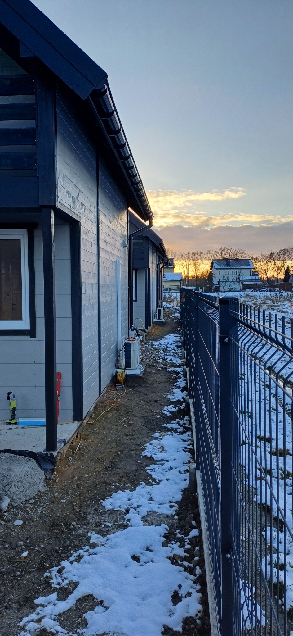 Zewnętrzne jednostki klimatyzacji zamontowane na ścianie budynku mieszkalnego w trakcie instalacji, widoczne narzędzia i przewody, częściowo ośnieżony teren.