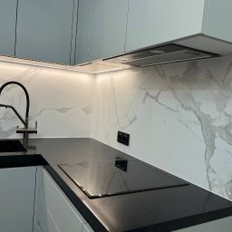 AN-BUD YURII NIKOLAIEV - Nowoczesna kuchnia z czarnym blatem, marmurową ścianą i oświetleniem LED pod szafkami, widoczny zlew z czarną baterią i płyta indukcyjna.