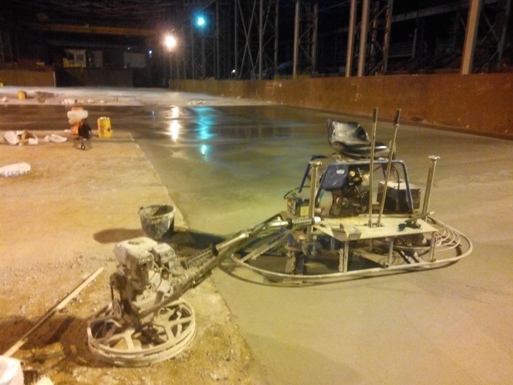 Zacieraczka do betonu podczas pracy na dużej powierzchni hali przemysłowej, widoczne ślady obróbki i mokra powierzchnia betonu w tle, w tle widoczna konstrukcja stalowa hali.