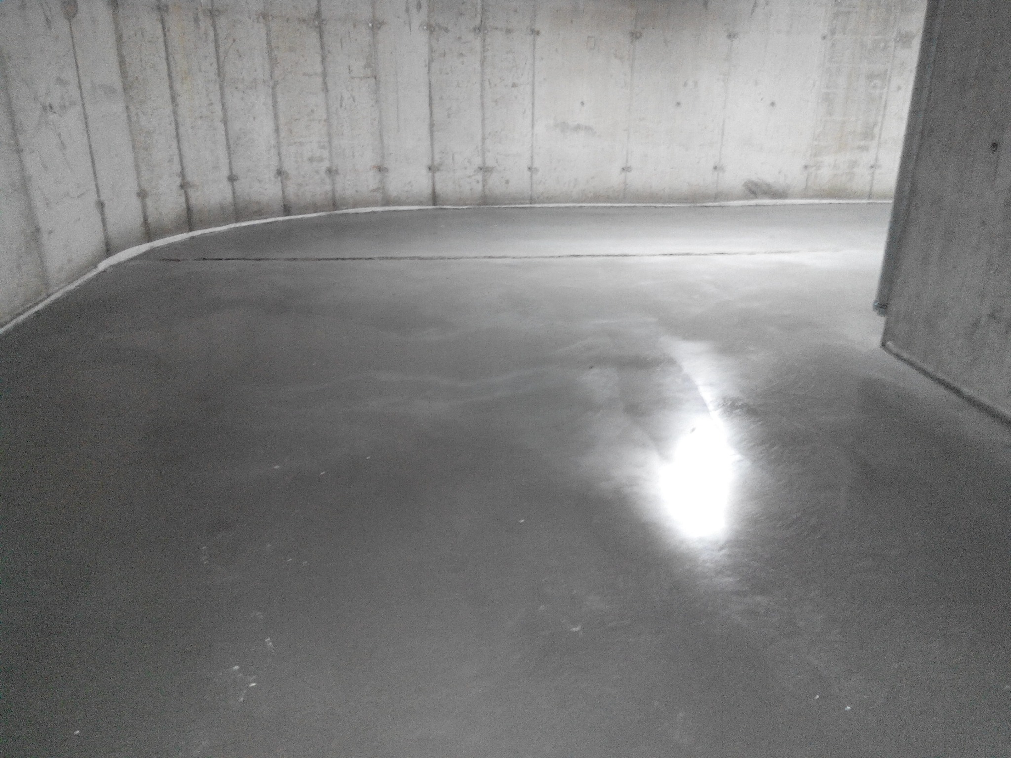 Świeżo wylana, gładka, szara posadzka w surowym, betonowym wnętrzu z widocznymi śladami po szalunkach na ścianach.