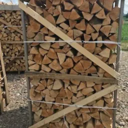 Układane w skrzyni pocięte kawałki drewna opałowego, zabezpieczone drewnianą ramą i sznurkiem.