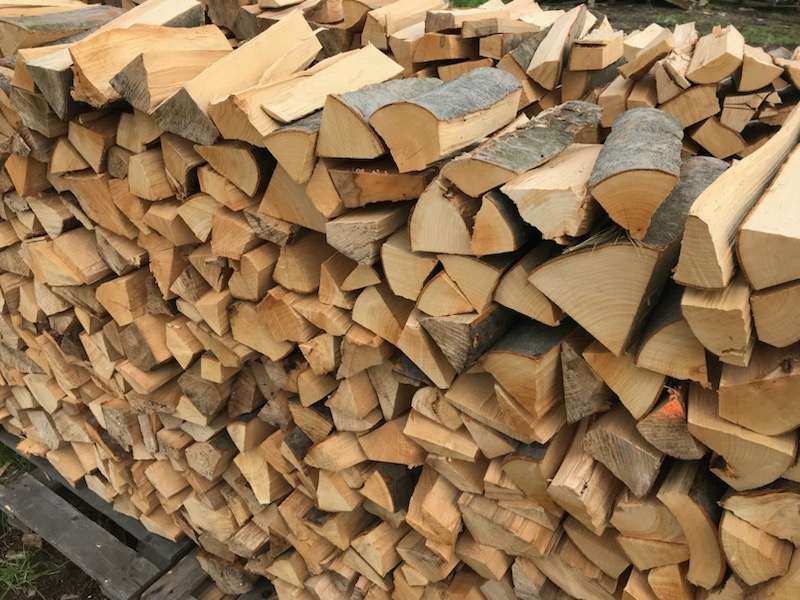 Stos pociętego drewna na palecie, widoczne sęki i kora na niektórych kawałkach.