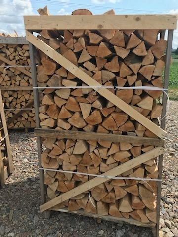 Układane w skrzyni pocięte kawałki drewna opałowego, zabezpieczone drewnianą ramą i sznurkiem.