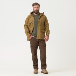 Luke Bochenek - Mężczyzna w brązowej kurtce z kapturem, zielonej koszulce i brązowych spodniach cargo, pozujący na białym tle, ręka w kieszeni.