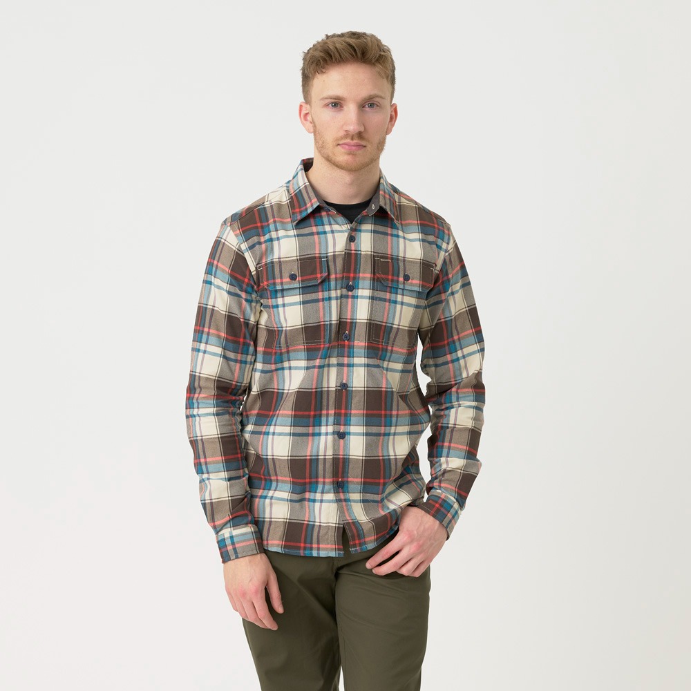 Mężczyzna o jasnych włosach prezentuje koszulę w kratę z przewagą brązów, błękitu i beżu na białym tle, ubrany w oliwkowe spodnie.