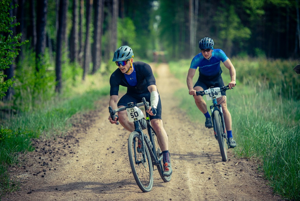 Dwóch kolarzy górskich rywalizuje na leśnej trasie w okolicach Brzegu Dolnego, z numerami startowymi na rowerach i kaskach, widok z przodu, reportaż z zawodów.