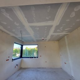 Wojciech Zjawinski - Surowy stan wnętrza: ściany i sufit po wstępnym pokryciu gładzią, widoczne łączenia płyt kartonowo-gipsowych na suficie, wystające przewody elektryczne, otwory pod gniazdka elektryczne w ścianach...