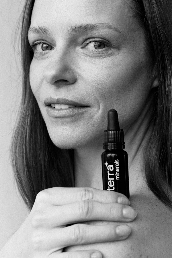 Kobieta z buteleczką olejku mineralnego Terra+ na tle twarzy, czarno-białe zdjęcie.