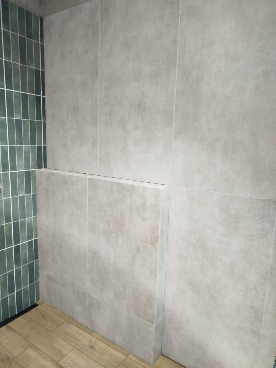 Wykończona łazienka z szarymi, wielkoformatowymi płytkami ściennymi i zielonymi płytkami w strefie prysznica, drewnopodobna podłoga.