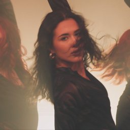 Dominik Ksel - Kobieta z rozwianymi włosami w czarnej sukience, w potrójnym ujęciu na rozmytym, ciepłym tle.