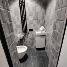 Nowoczesna łazienka w odcieniach szarości z geometrycznymi płytkami na ścianach, wiszącą toaletą, szafką z umywalką i czarnym grzejnikiem drabinkowym.