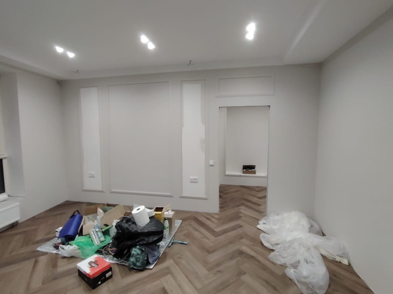 Pokój w trakcie remontu: świeżo pomalowane ściany w odcieniach bieli, drewniana podłoga ułożona w jodełkę, widoczne ślady prac remontowych i narzędzia.