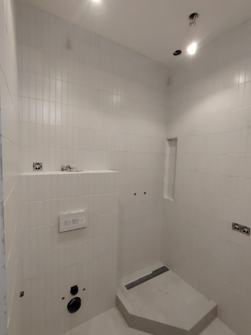 Wnętrze łazienki w trakcie wykańczania, białe pionowe płytki, odpływ liniowy w brodziku, przygotowane punkty instalacyjne.