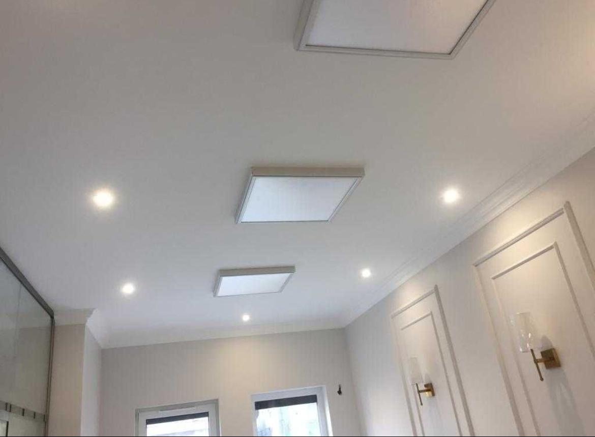 Nowoczesne oświetlenie sufitowe z panelami LED i punktowymi lampami halogenowymi w jasnym wnętrzu z dekoracyjnymi listwami ściennymi.