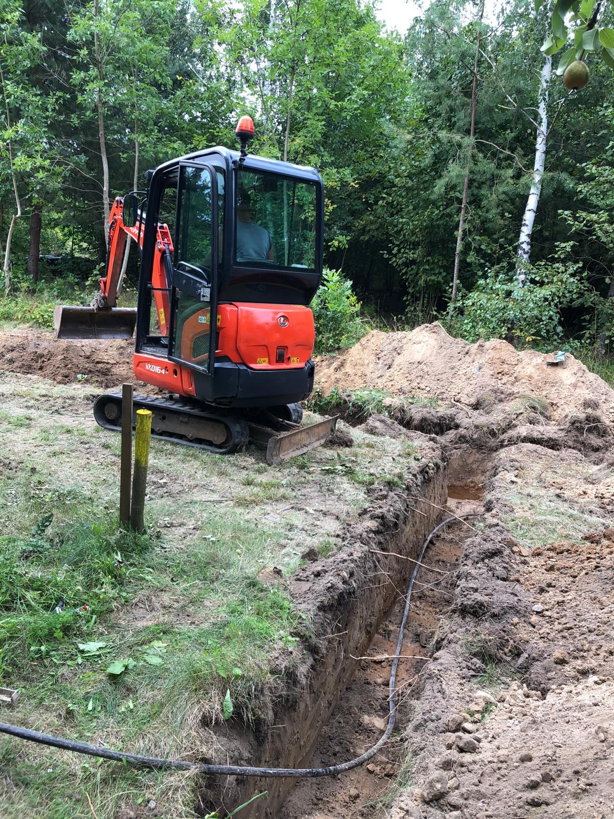 Wykop pod kabel elektryczny w ziemi, wykonany minikoparką Kubota KX016-4 w Zielonej Górze, widoczne żółto-czarne słupki wyznaczające trasę.