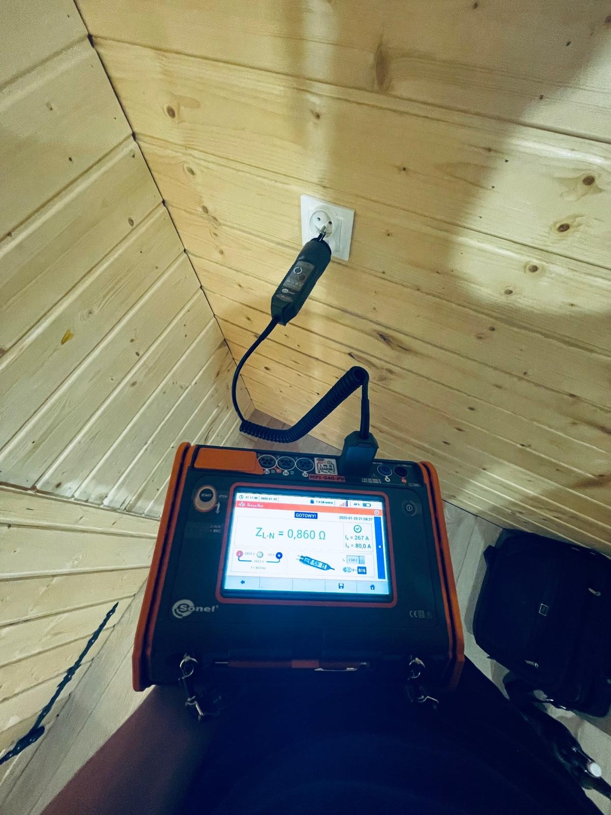 Miernik Sonel MP2-540-PV podłączony do gniazdka elektrycznego w pomieszczeniu wykończonym drewnem, wskazujący impedancję pętli zwarcia ZL-N równą 0,860 Ω.