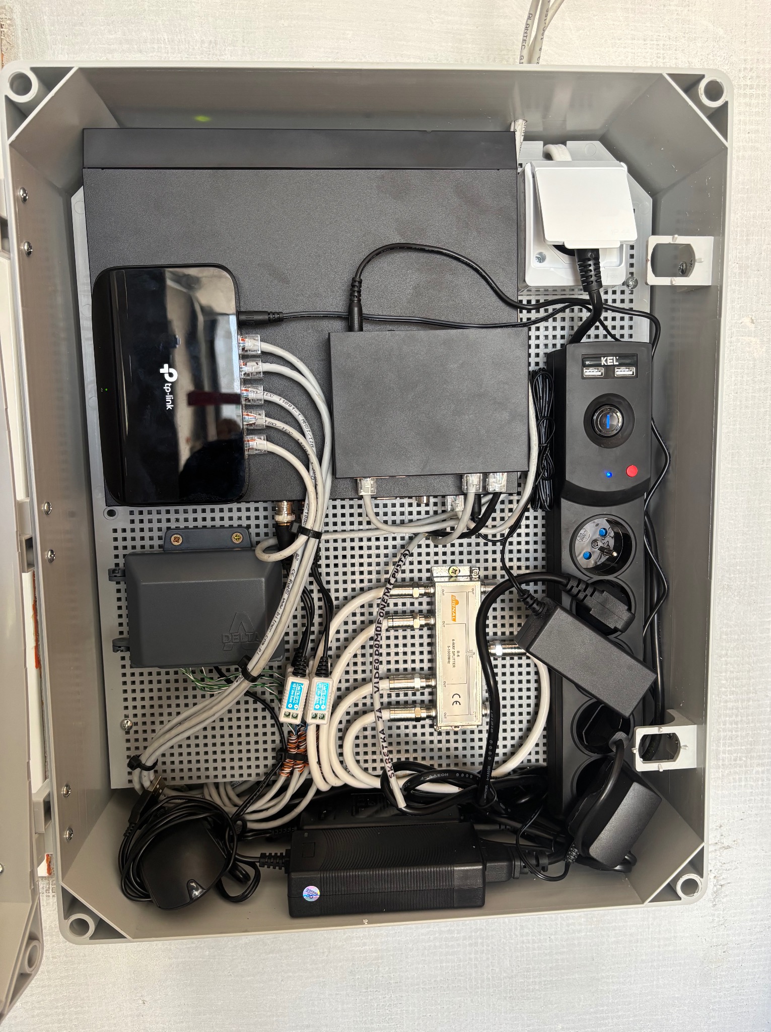 Szafka z elementami instalacji monitoringu, routerem TP-Link, rozgałęźnikiem antenowym Signal, listwą zasilającą KEL i przewodami. Kompaktowe rozwiązanie.