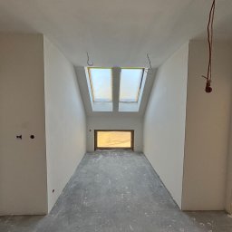 Finezja Wykończeń Krzysztof Chrobak - Wnętrze poddasza po gładziowaniu ścian i sufitu, z oknami dachowymi zabezpieczonymi folią i surową podłogą. Widoczne kable i puszki elektryczne.