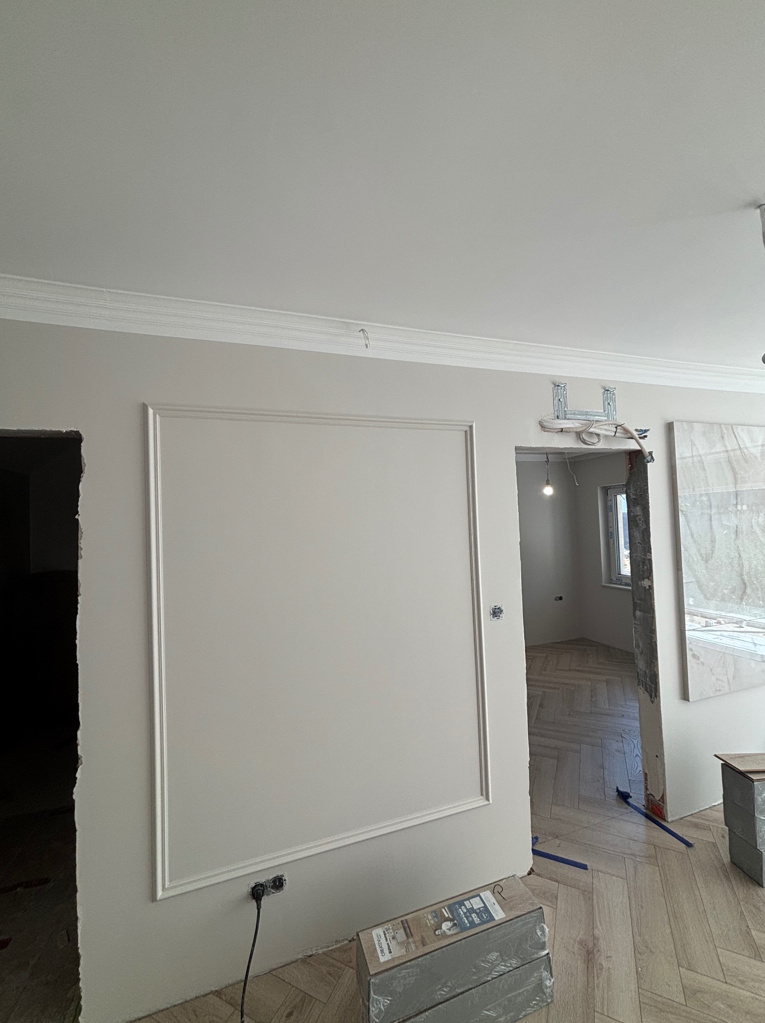 Eleganckie wykończenie ścian z dekoracyjnymi listwami i gładką powierzchnią. Parkiet w jodełkę. Fragment instalacji elektrycznej i przygotowania do montażu drzwi.