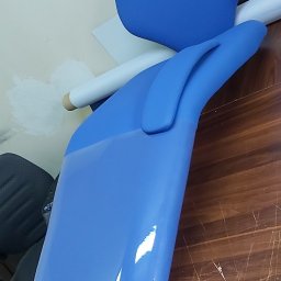 PRACOWNIA TAPICERSKA Wojciech Czapnik - Niebieskie, błyszczące elementy fotela stomatologicznego na drewnianym blacie, widoczne ślady pracy na ścianie w tle.