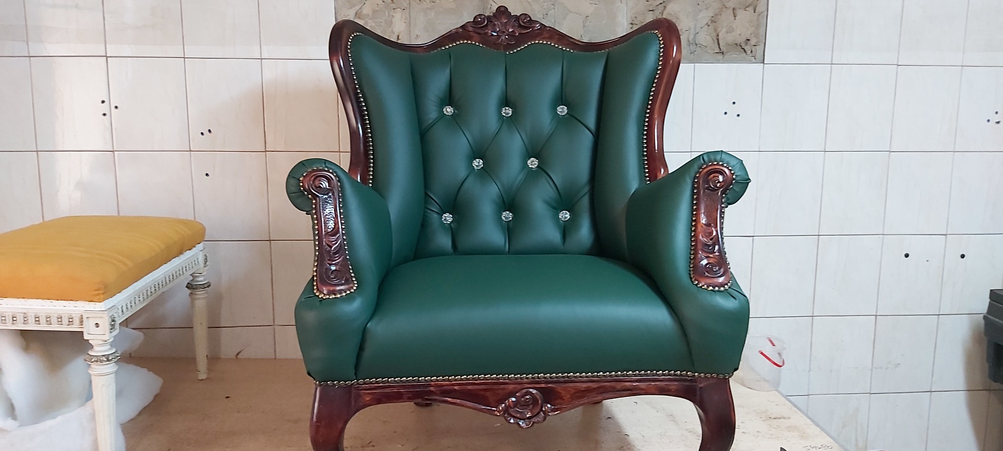 Odnowiony, zielony fotel typu uszak z kryształkami i ciemnobrązowymi, rzeźbionymi elementami drewnianymi, widoczny w Czechowicach-Dziedzicach, obok znajduje się żółty taboret na białych nogach.