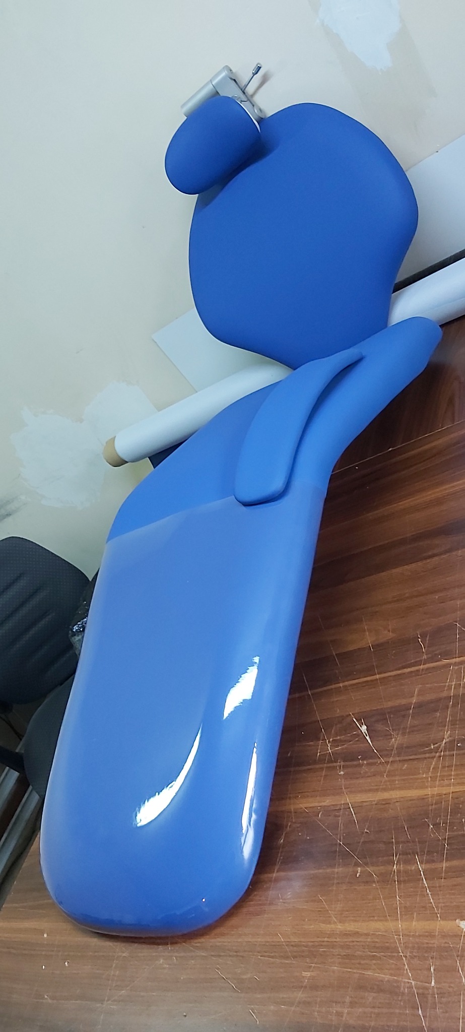 Niebieskie, błyszczące elementy fotela stomatologicznego na drewnianym blacie, widoczne ślady pracy na ścianie w tle.