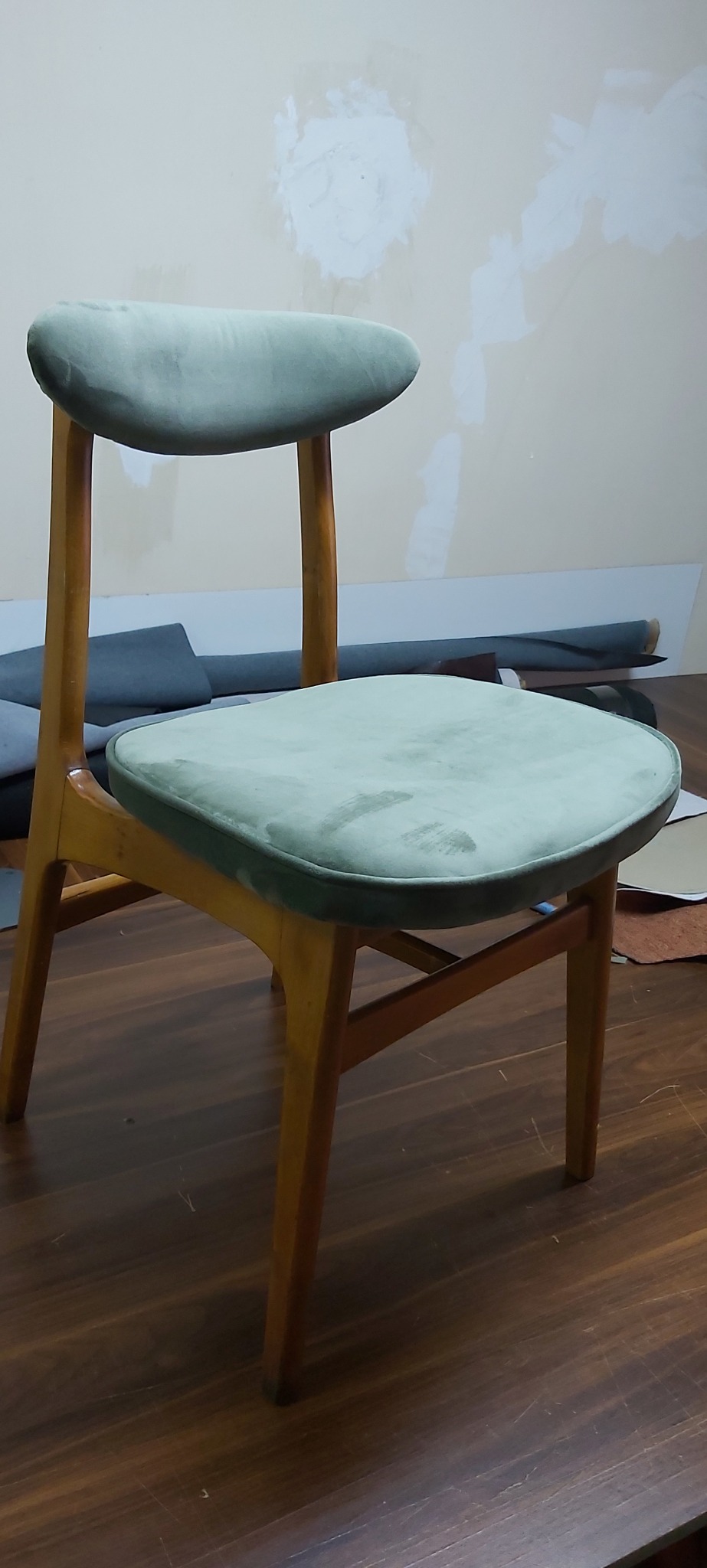 Drewniane krzesło z odnowionym, jasnozielonym welurowym siedziskiem i oparciem, widoczne ślady użytkowania na siedzisku, w tle materiały tapicerskie