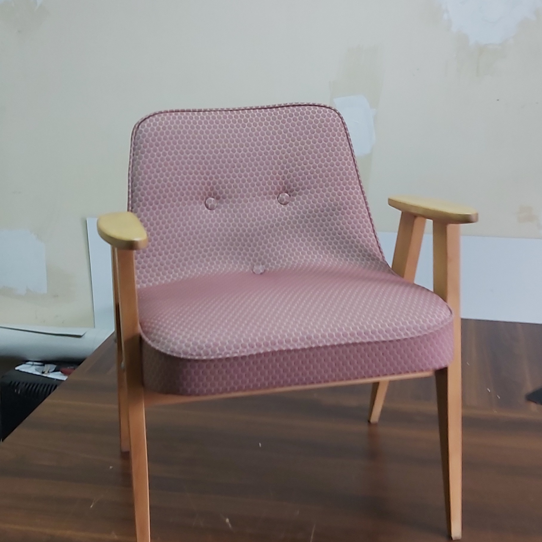 Odnowiony fotel z tapicerką w różowe kropki i jasnymi drewnianymi nogami, widoczne trzy guziki na oparciu.