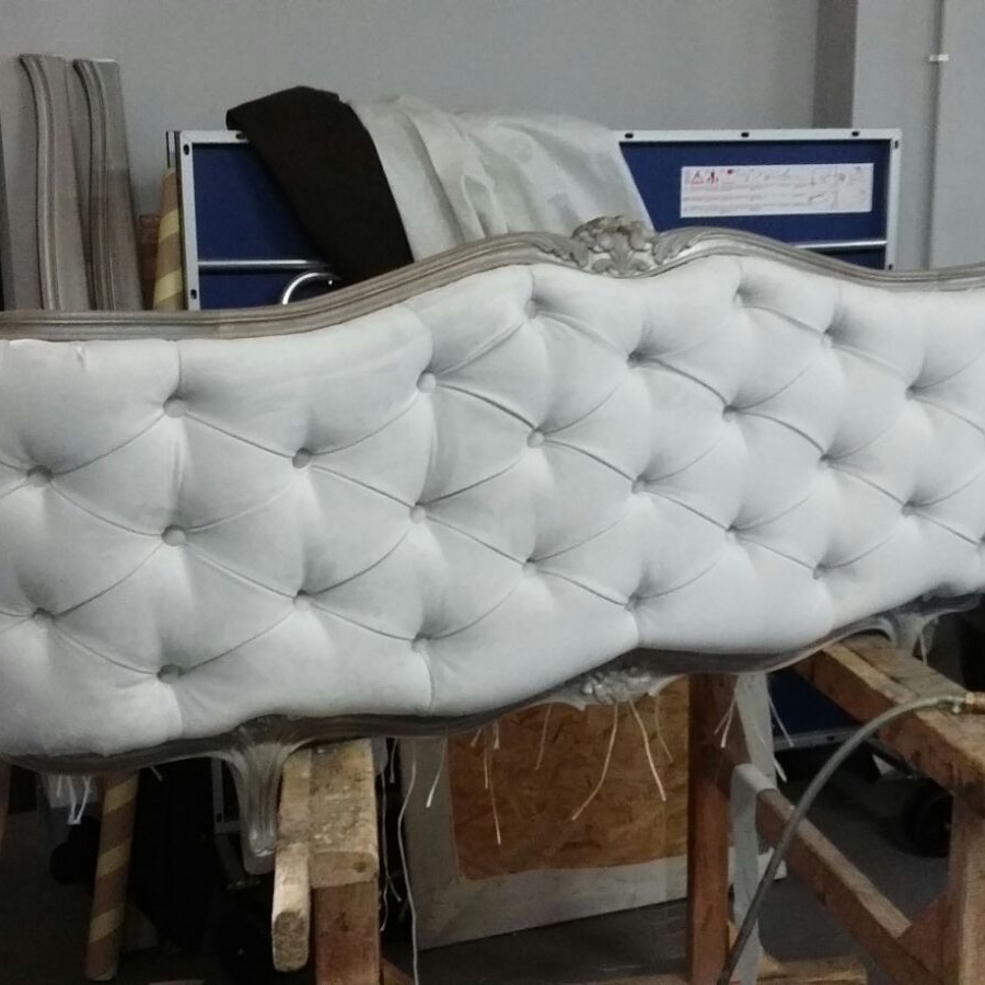 Biały, pikowany zagłówek łóżka w stylu vintage, z srebrną ramą, na drewnianym stelażu w warsztacie.