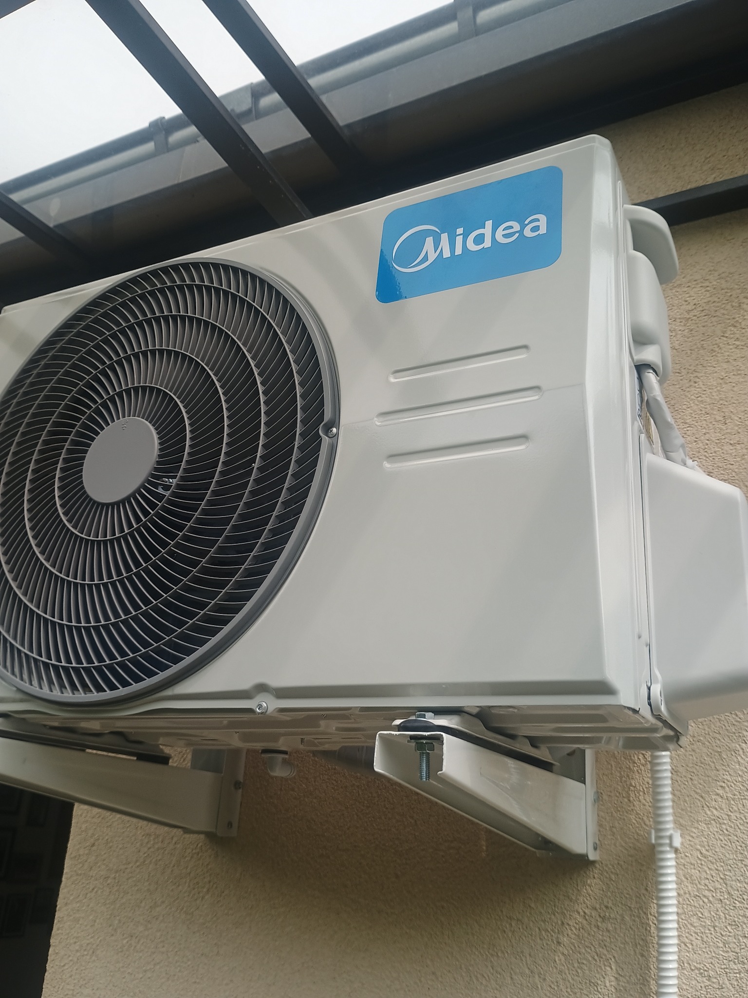 Zamontowana jednostka zewnętrzna klimatyzacji Midea na elewacji budynku w Świdniku. Widoczne mocowania i przewody. Ujęcie z dołu, lekko z prawej strony.