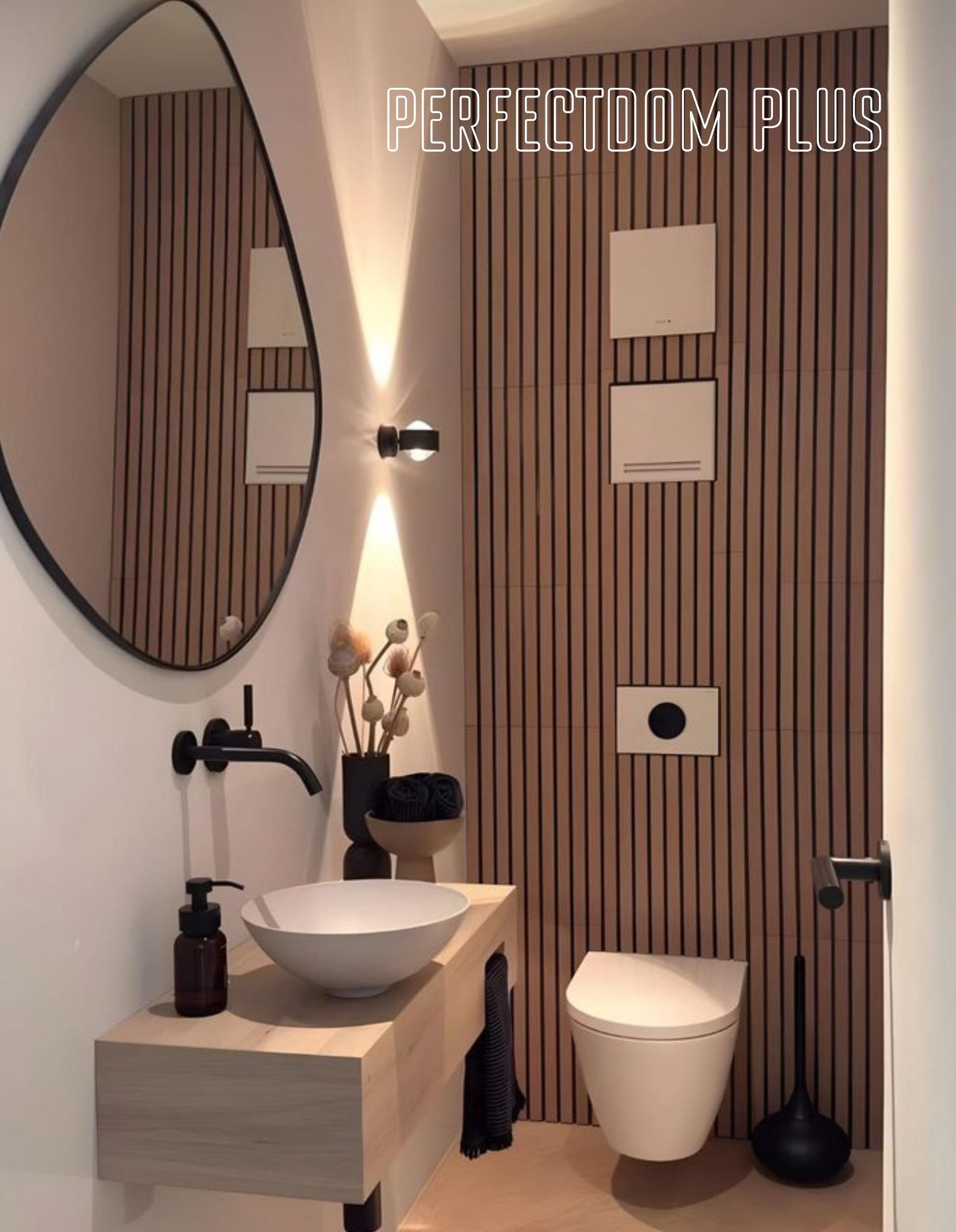 Nowoczesna łazienka z drewnianymi lamelami na ścianie, owalnym lustrem z czarną ramą, białą umywalką nablatową i czarną armaturą oraz wiszącą miską WC.