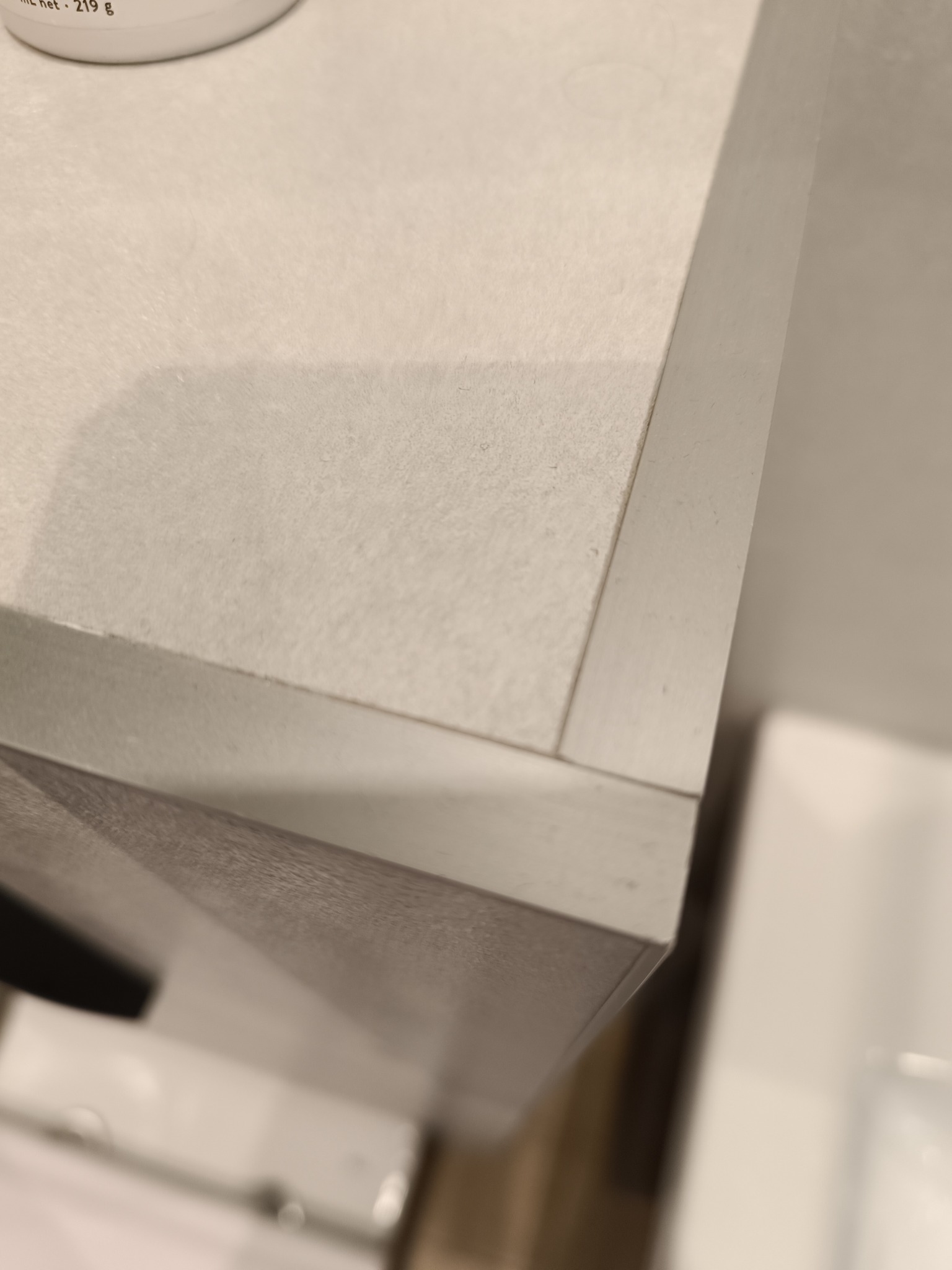 Detal narożnika szafki kuchennej z blatem wykończonym jasnoszarym materiałem imitującym kamień, widoczna krawędź blatu i front szafki, ujęcie z góry pod kątem.