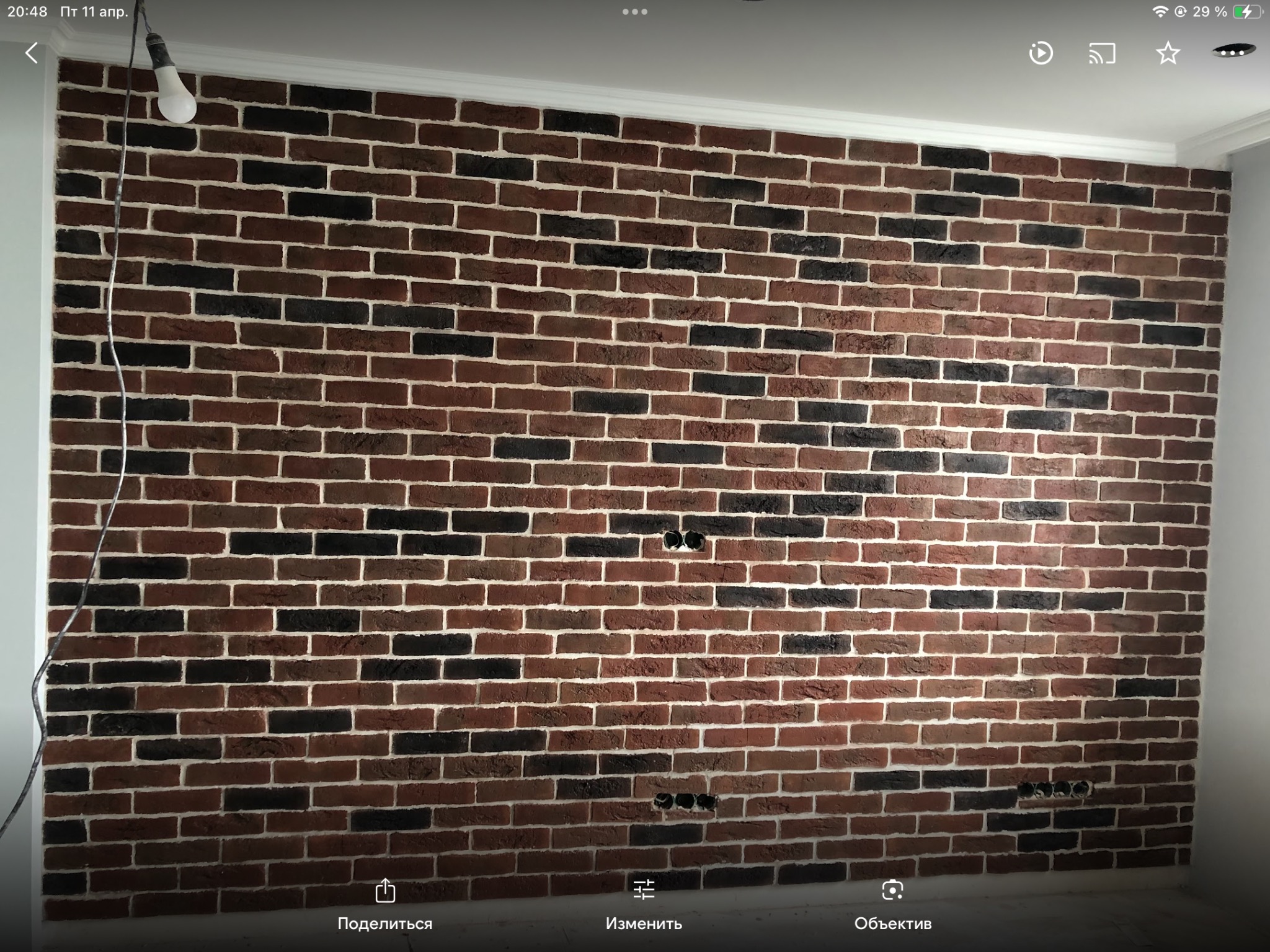 Ściana wykończona klinkierem w odcieniach brązu i czerni z białymi fugami, widoczne puszki elektryczne i tymczasowe oświetlenie.