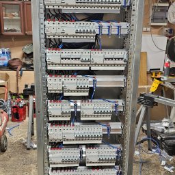 MARCIN BOŁOZ - Rozdzielnica elektryczna w metalowej obudowie, widok z przodu. Liczne zabezpieczenia i okablowanie. Instalacja wykonana w schludny sposób.