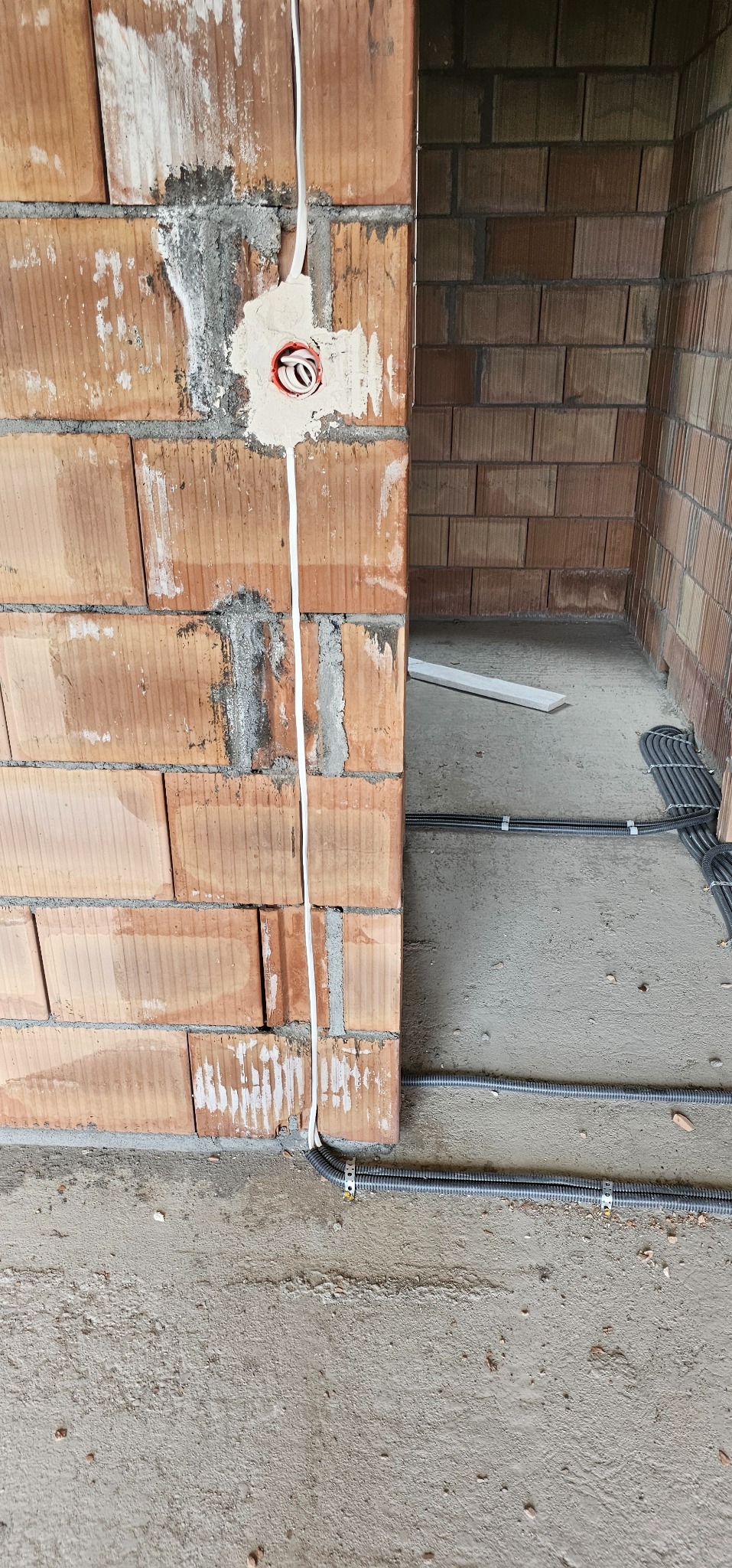 Instalacja elektryczna w trakcie budowy: kable w peszlach prowadzone po podłodze, puszka elektryczna w surowej ścianie z cegły dziurawki.