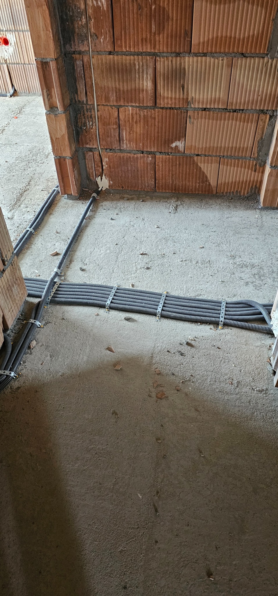 Rury instalacyjne w peszlach, przymocowane do podłoża w surowym stanie, widoczne na tle ścian z cegły dziurawki, przed wylaniem posadzki.