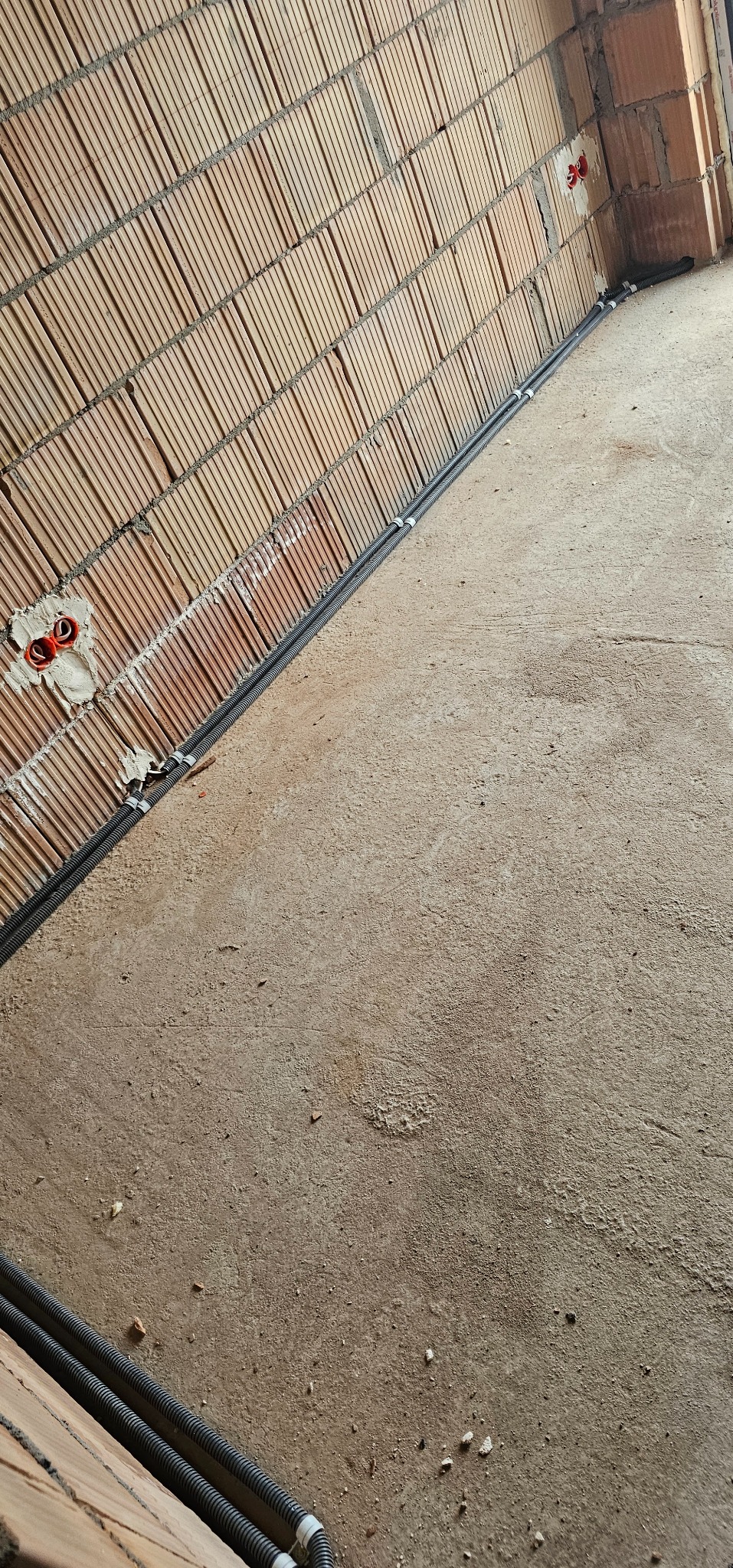 Murowana ściana z korytkami na przewody elektryczne i peszlami. Widoczne puszki instalacyjne. Surowy stan, przygotowanie do dalszych prac wykończeniowych.