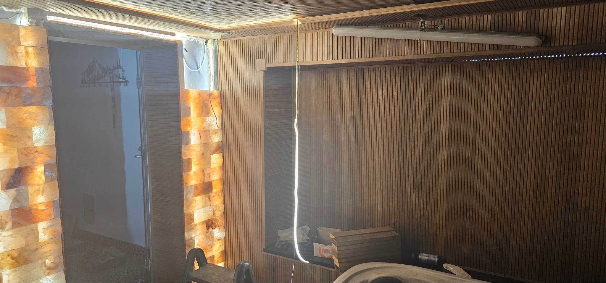 Wykończenie wnętrza sauny z drewnianą boazerią, oświetleniem LED i elementami z bloków solnych. Widoczna lampa sufitowa i akcesoria.