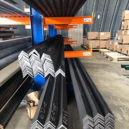 APHD D.M.K. KAWIŃSCY SPÓŁKA CYWILNA - Stalowe kątowniki z białymi oznaczeniami na regale magazynowym, widoczne palety z kartonami w tle.