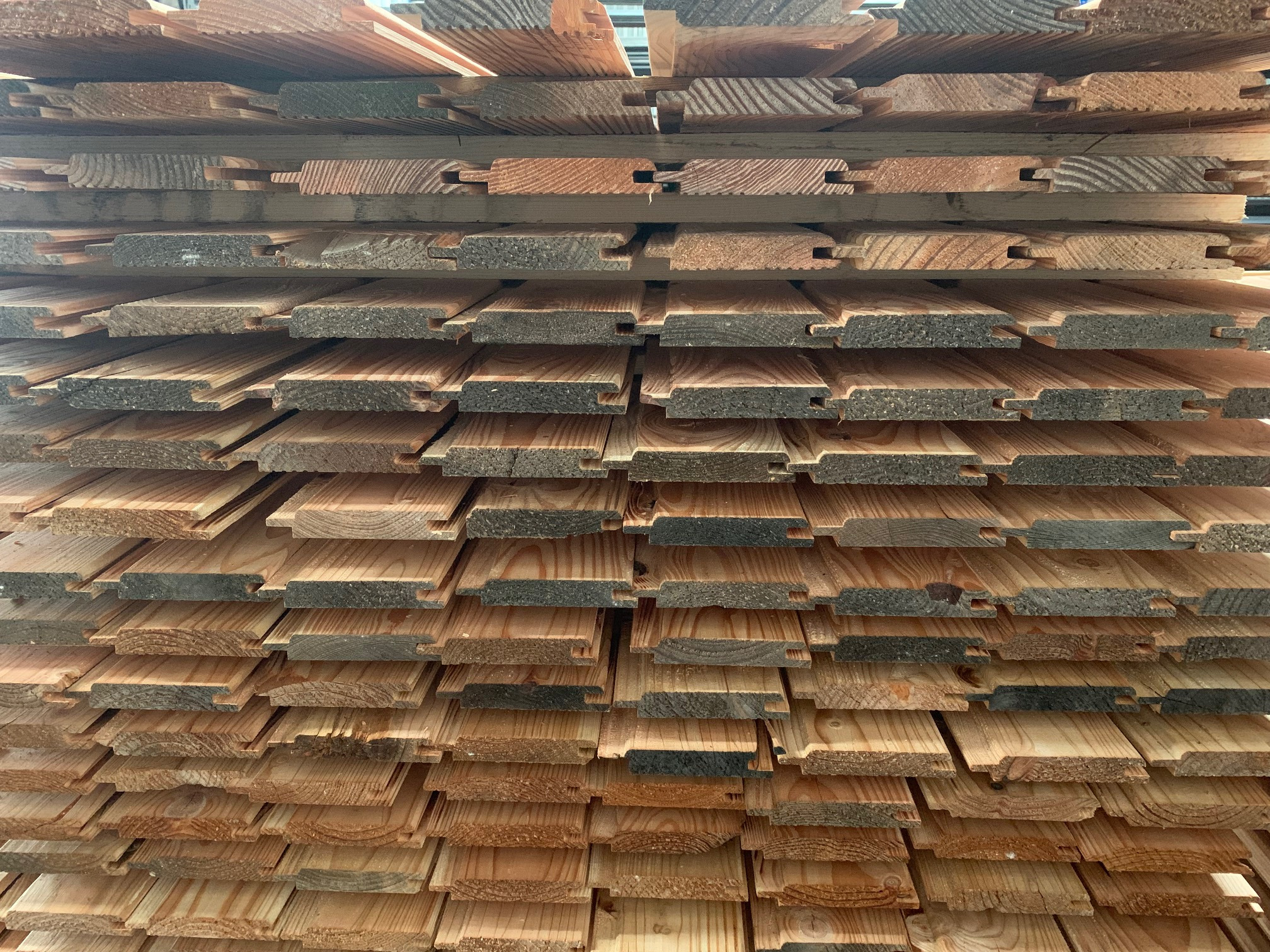 Stos desek z wyfrezowanymi wpustami i wypustkami, ułożonych warstwami; widoczny przekrój drewna i jego naturalne usłojenie.