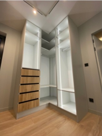 Narożna szafa wnękowa z oświetleniem LED i drewnianymi szufladami, widok z dołu, podkreślający przestronność i nowoczesny design.