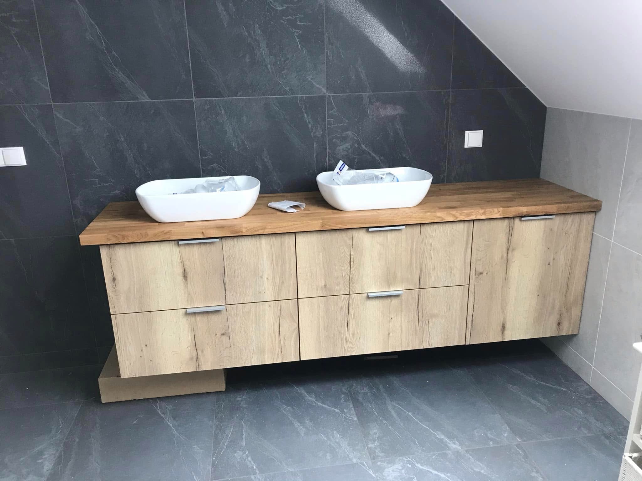 Łazienka w szarościach: drewniana szafka pod umywalki nablatowe, marmurowe płytki na ścianach i podłodze. Ukośny sufit dodaje charakteru.